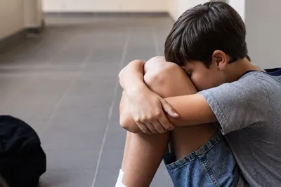 bullying_nino_solo_llorando_shogun_jiujitsu_queretaro_400x267 Nino se encuentra sentado en el piso abrazando sus rodillas, ocultando el rostro en un gesto de tristeza y aislamiento.