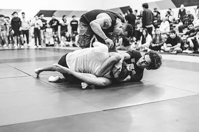 Atletas compiten en torneo de grappling bajo supervision de referee en tatami de Shogun Jiujitsu Dojo.